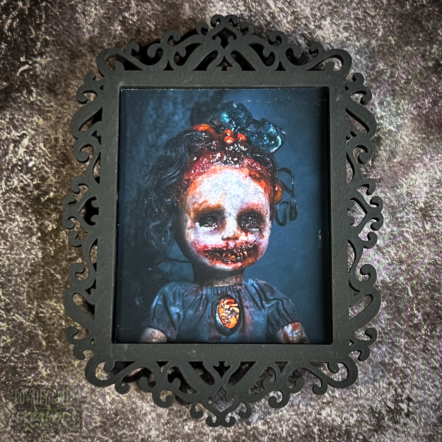 A gothic-style framed art print featuring a dark, eerie photograph of a grotesque doll-like figure.