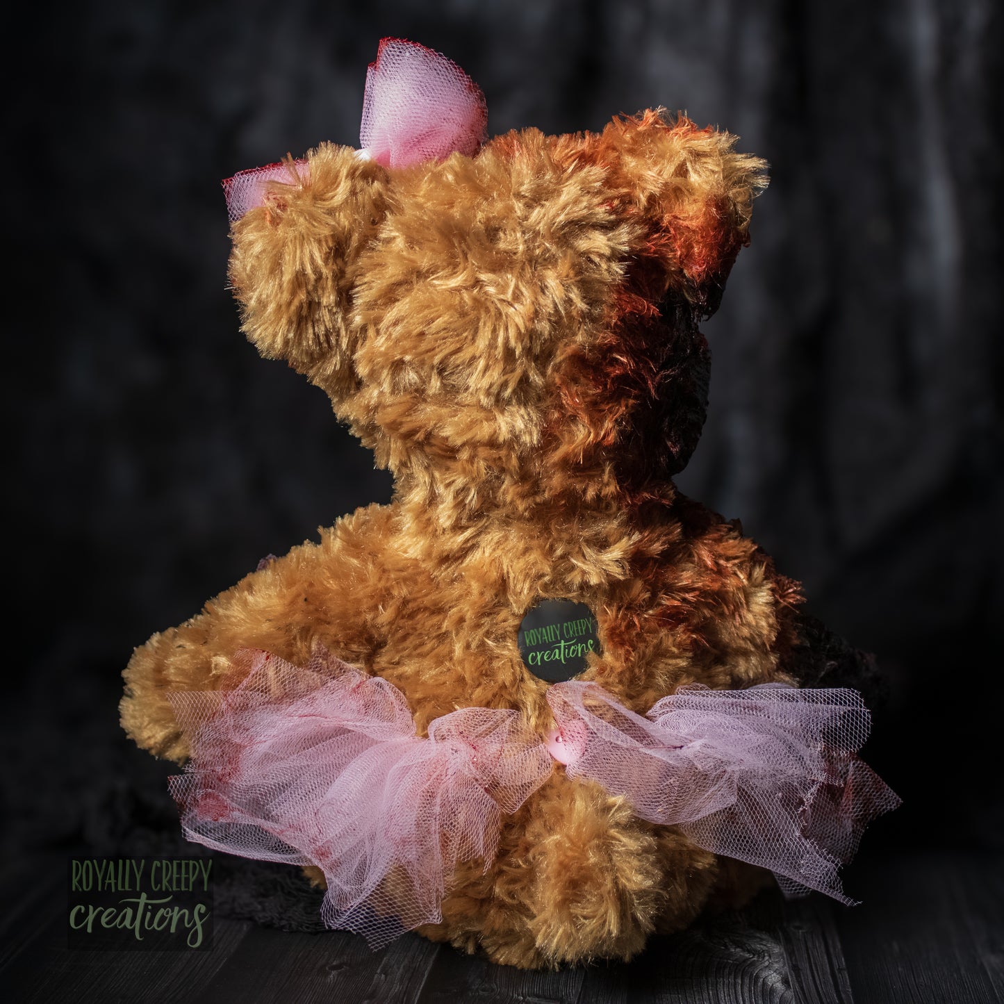 Backside view of horror teddy bear wearing a tutu & bow and a "Royally Creepy Creations" logo.