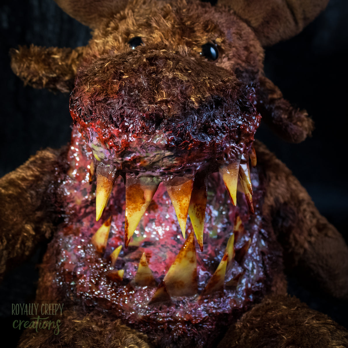 A close-up of a creepy moose plush toy with a horror zombie-like mouth, showing exposed flesh and sharp yellowed teeth, set against a dark textured background.