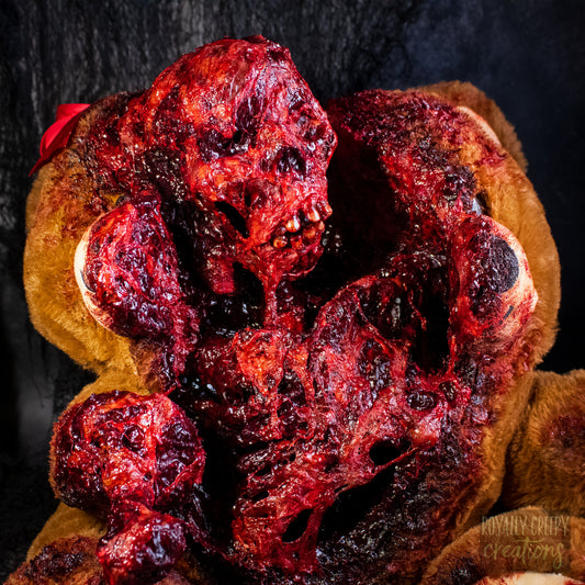 A close-up of a horror-themed plush teddy bear that is split down the middle and a gory bloody skeleton is emerging from it's opening.