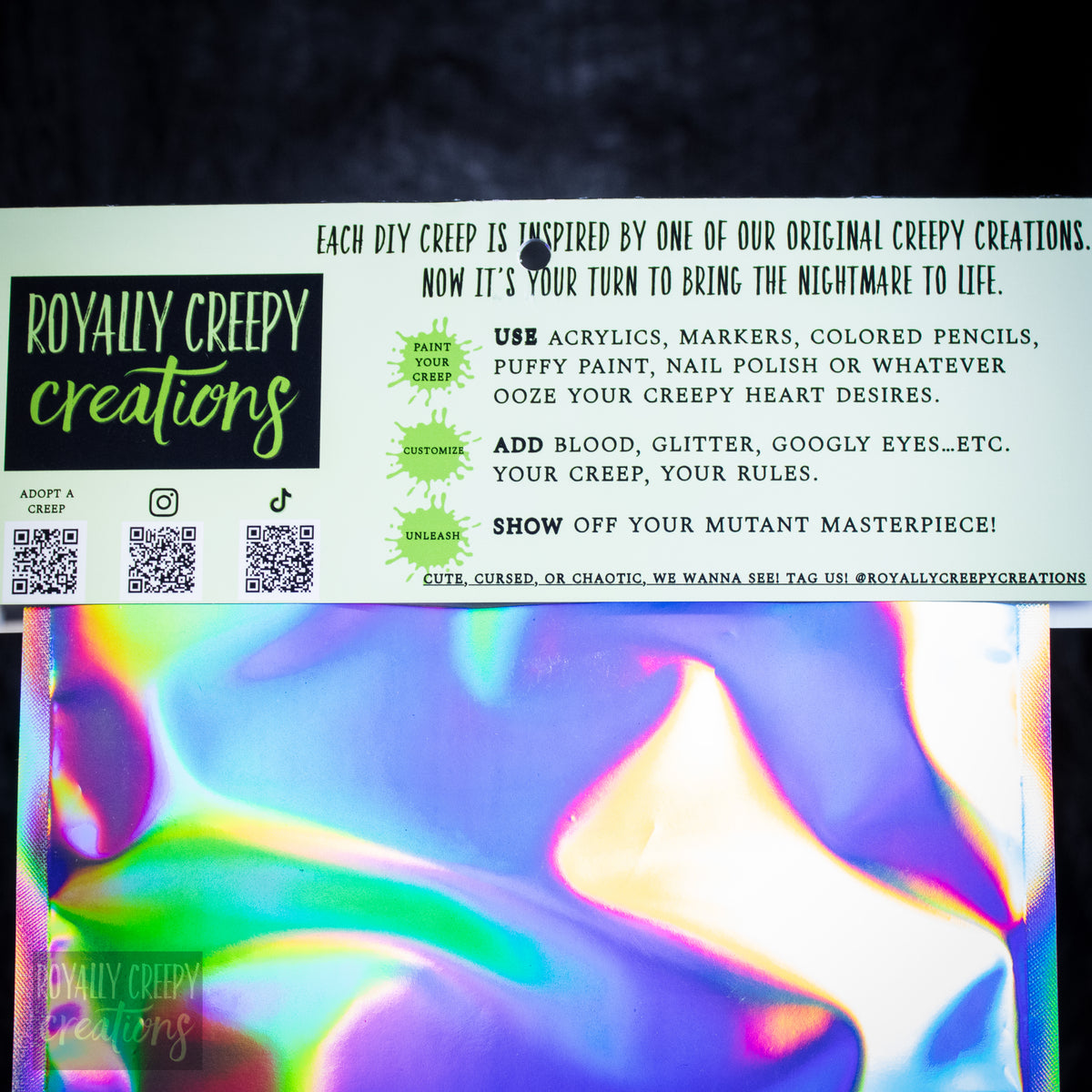 A printed DIY creep design card from Royally Creepy Creations above a colorful iridescent surface. The card includes text instructions, QR codes, and the Royally Creepy Creations logo.