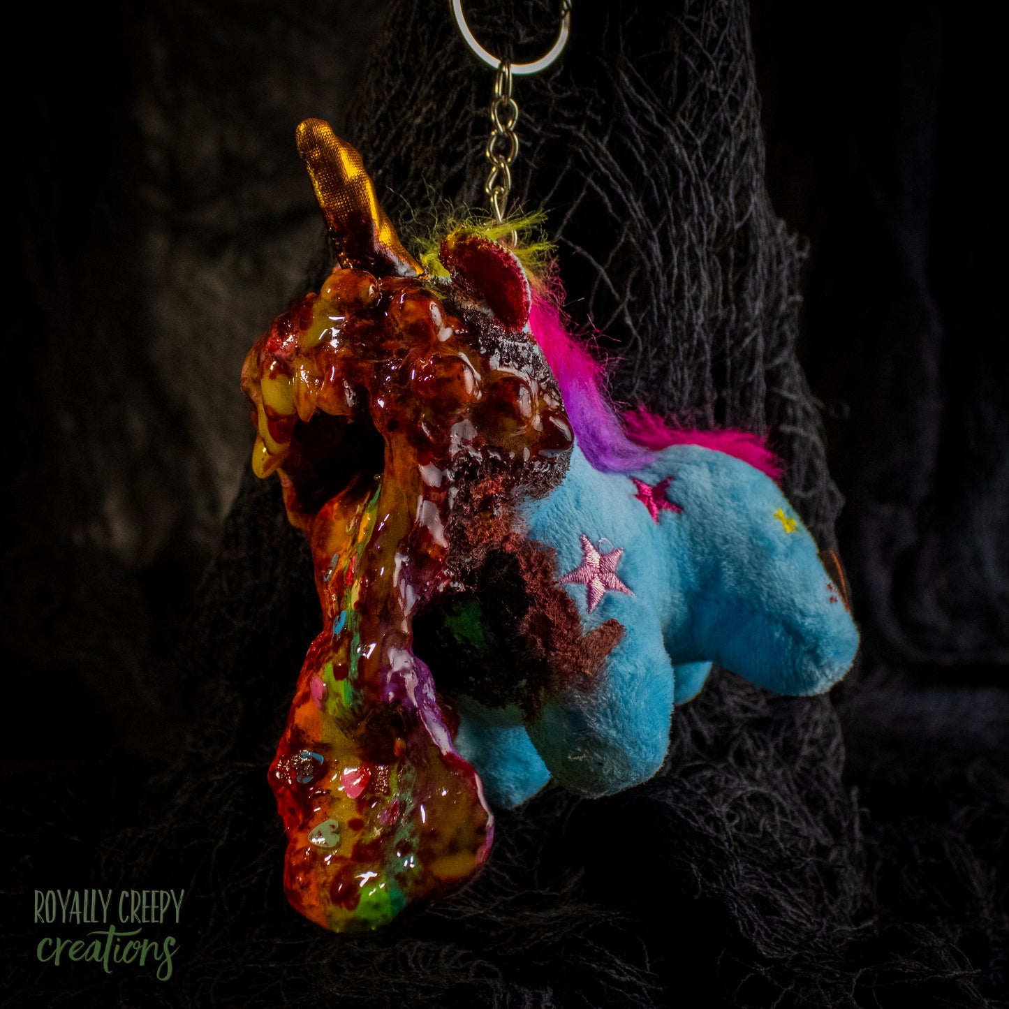 A creepy, horror-themed keychain featuring a plush unicorn vomiting up a rainbow.