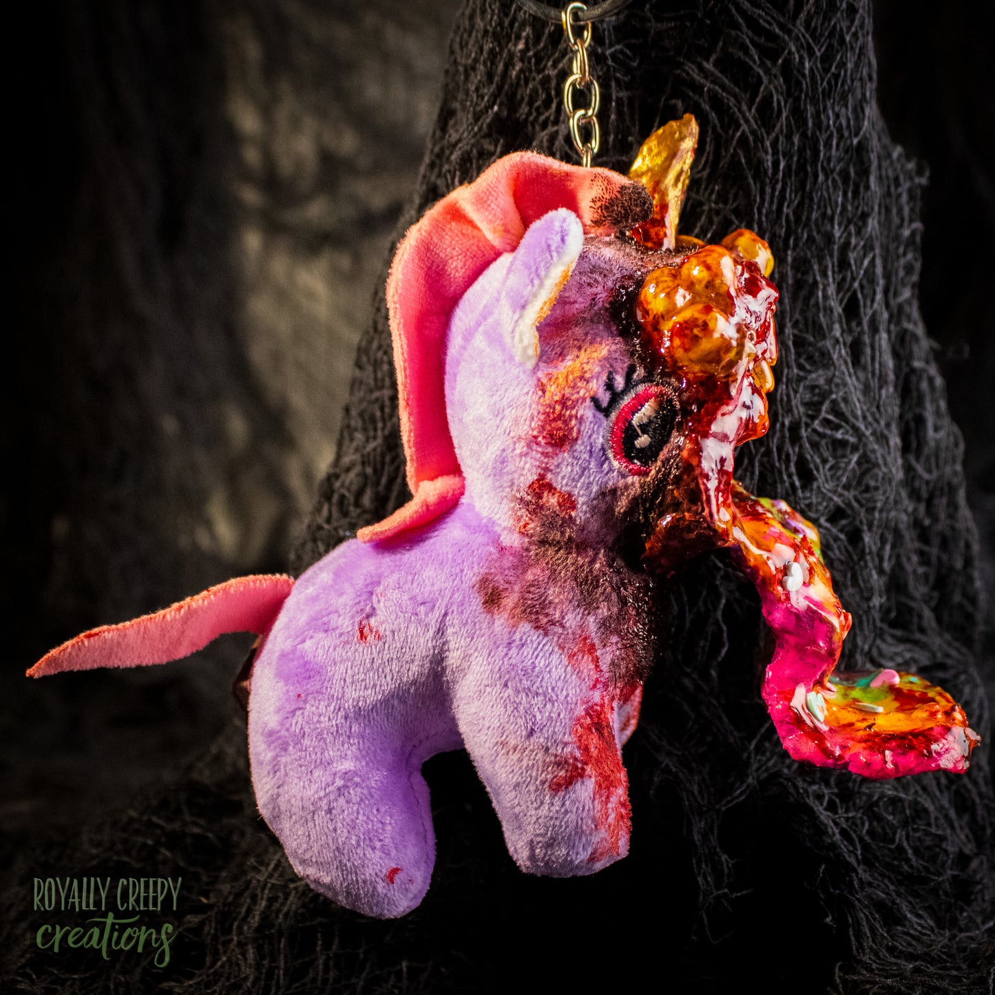 A creepy, horror-themed keychain featuring a plush unicorn vomiting up a rainbow.