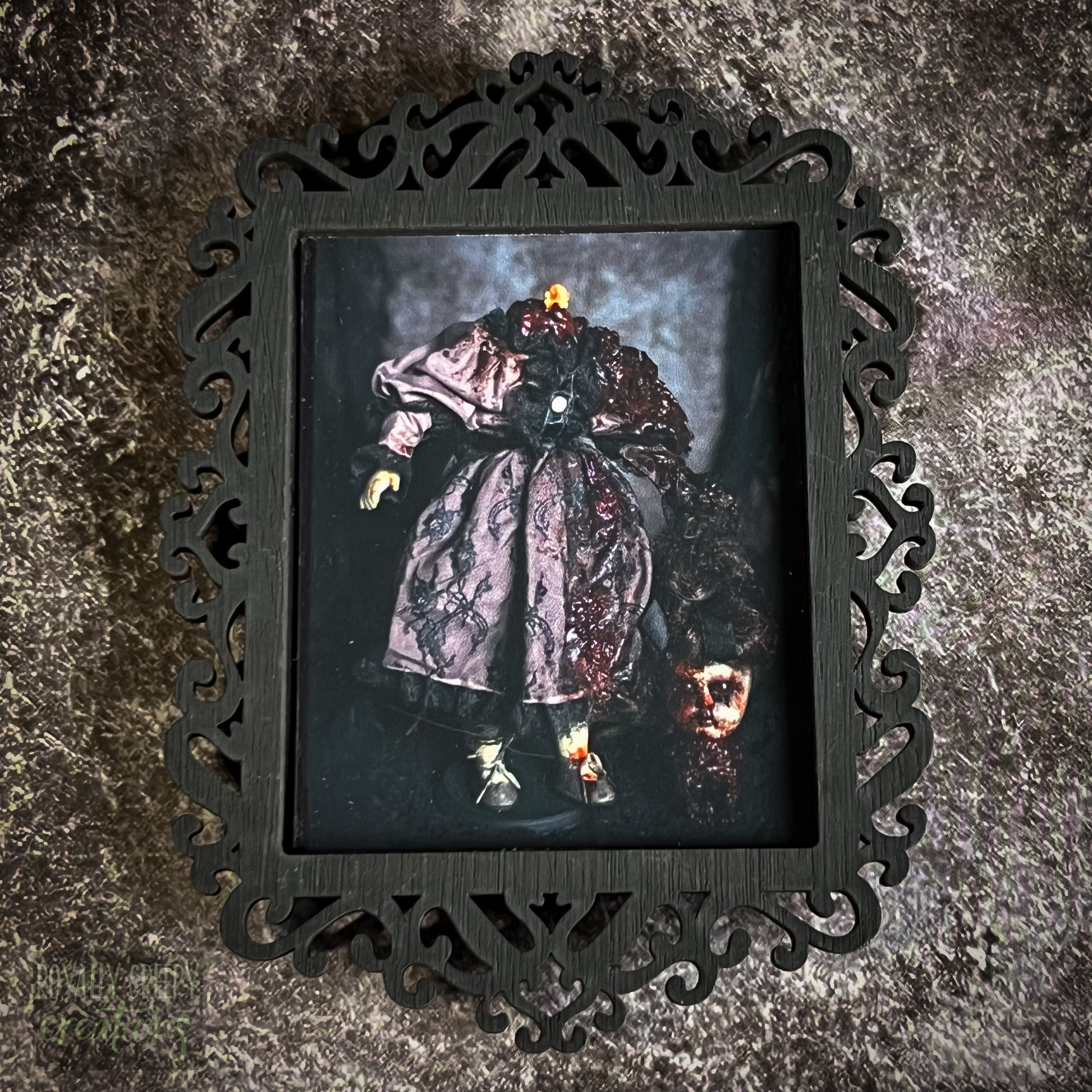 A gothic-style framed art print featuring a dark, eerie illustration of a grotesque doll-like figure.