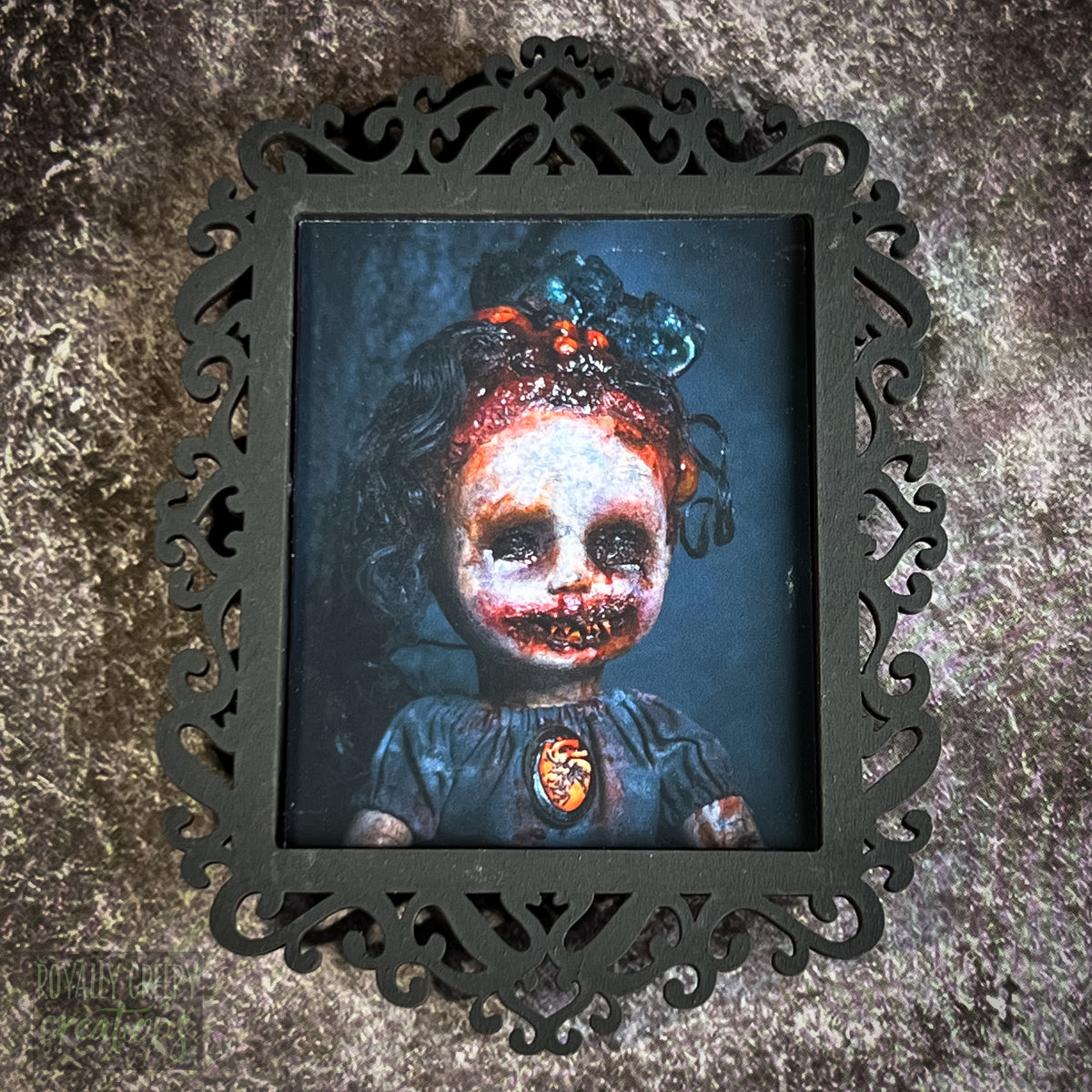 A gothic-style framed art print featuring a dark, eerie photograph of a grotesque doll-like figure.