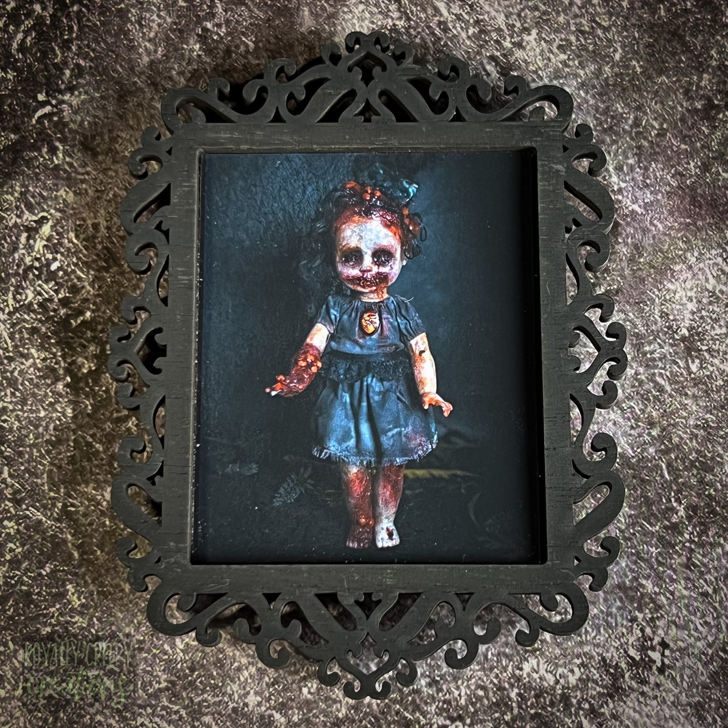 A gothic-style framed art print featuring a dark, eerie photograph of a grotesque doll-like figure.