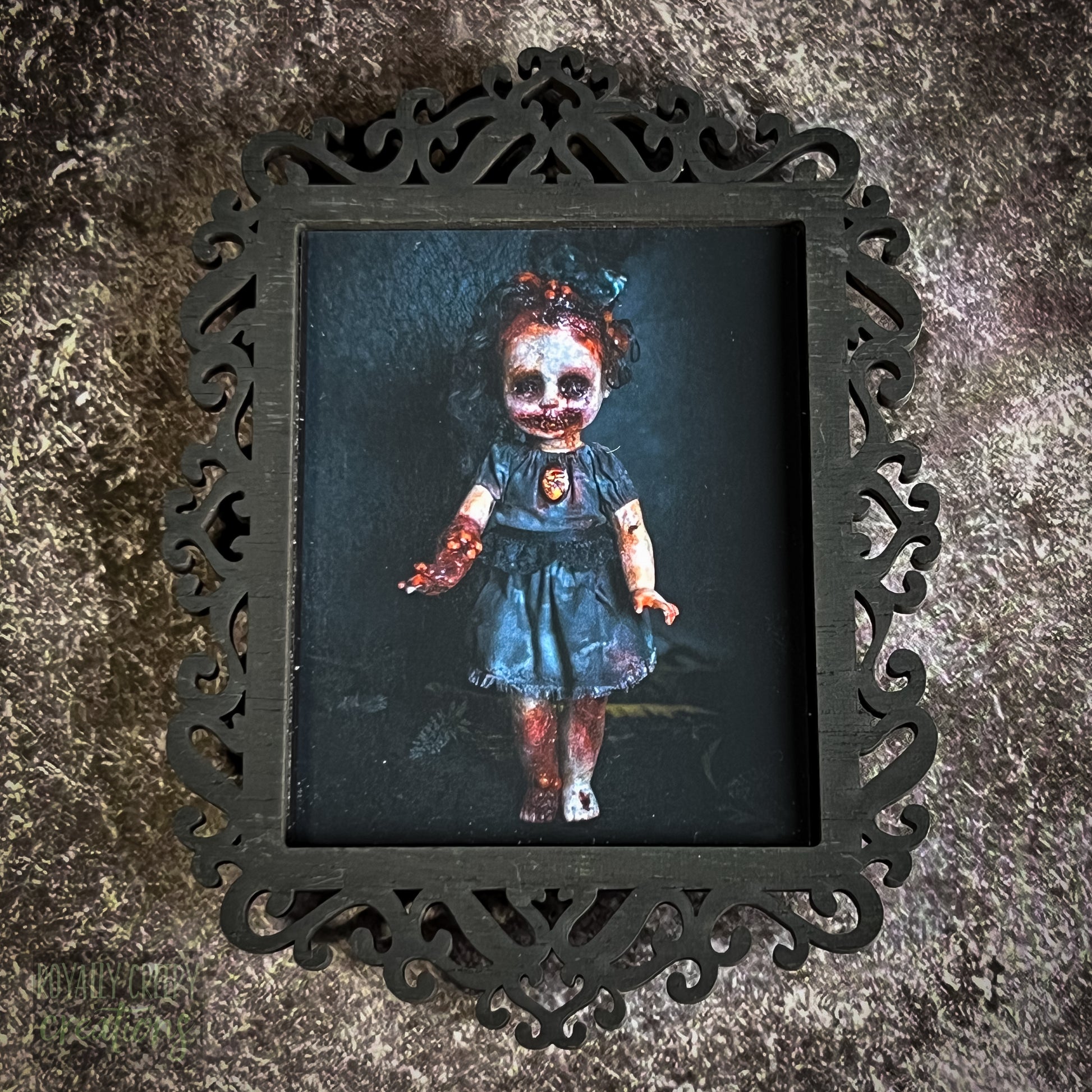 A gothic-style framed art print featuring a dark, eerie photograph of a grotesque doll-like figure.