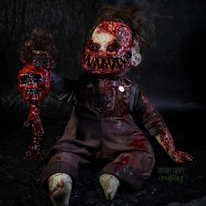 A creepy, horror-themed doll with a big smile full of sharp teeth and a blood-splattered face, dark tattered hair, and a severed skull in it's hand, posed against a dark textured background.