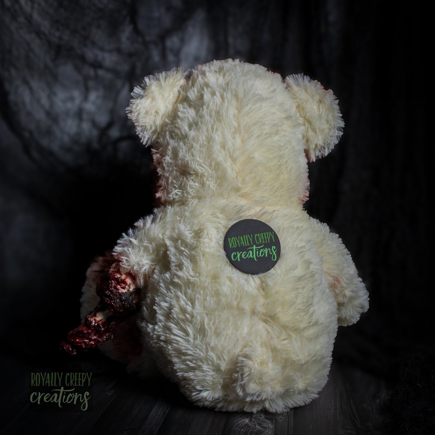 Back side of white teddy bear with a "Royally Creepy Creations" logo.