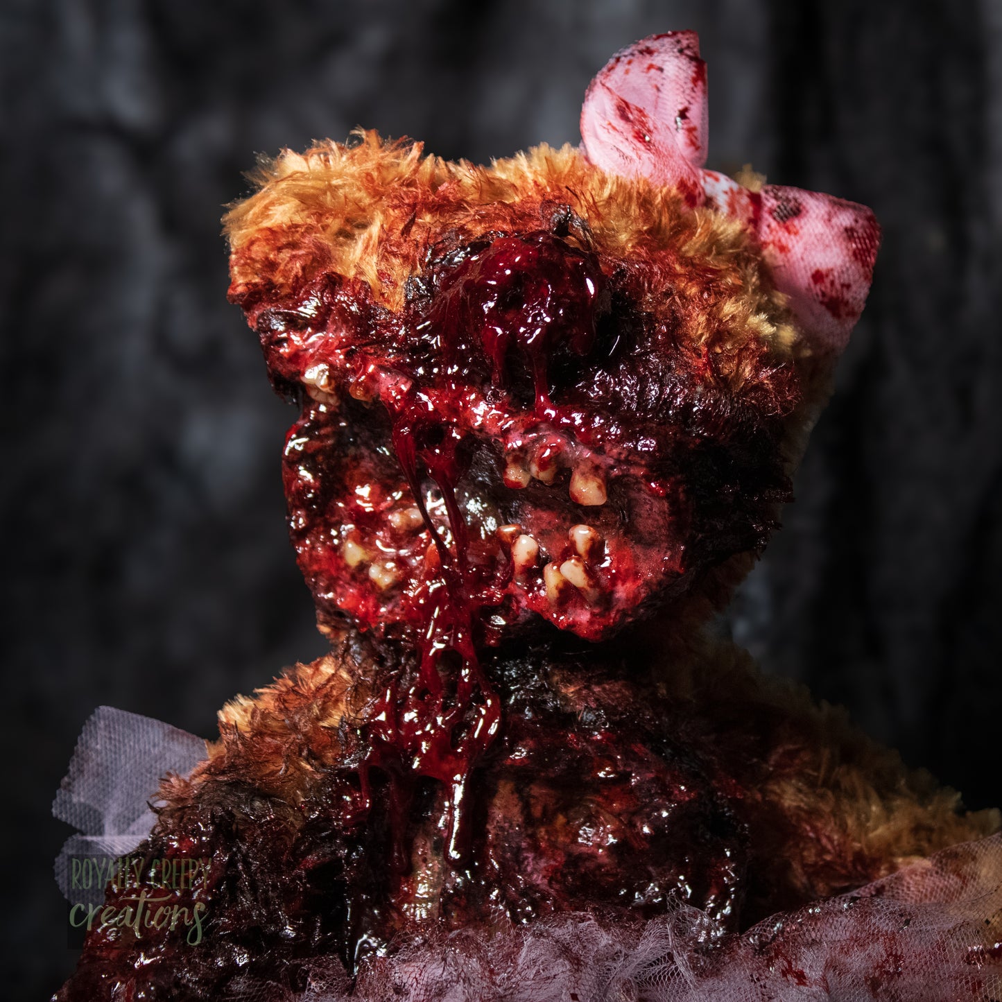 Close-up of horror teddy bear with exposed teeth, wearing a tutu & bow.