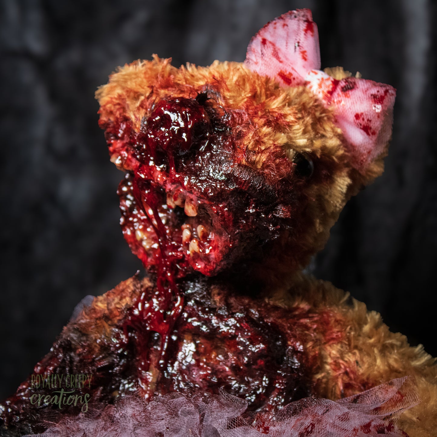 Front view close-up of horror teddy bear with exposed teeth, wearing a tutu & bow.