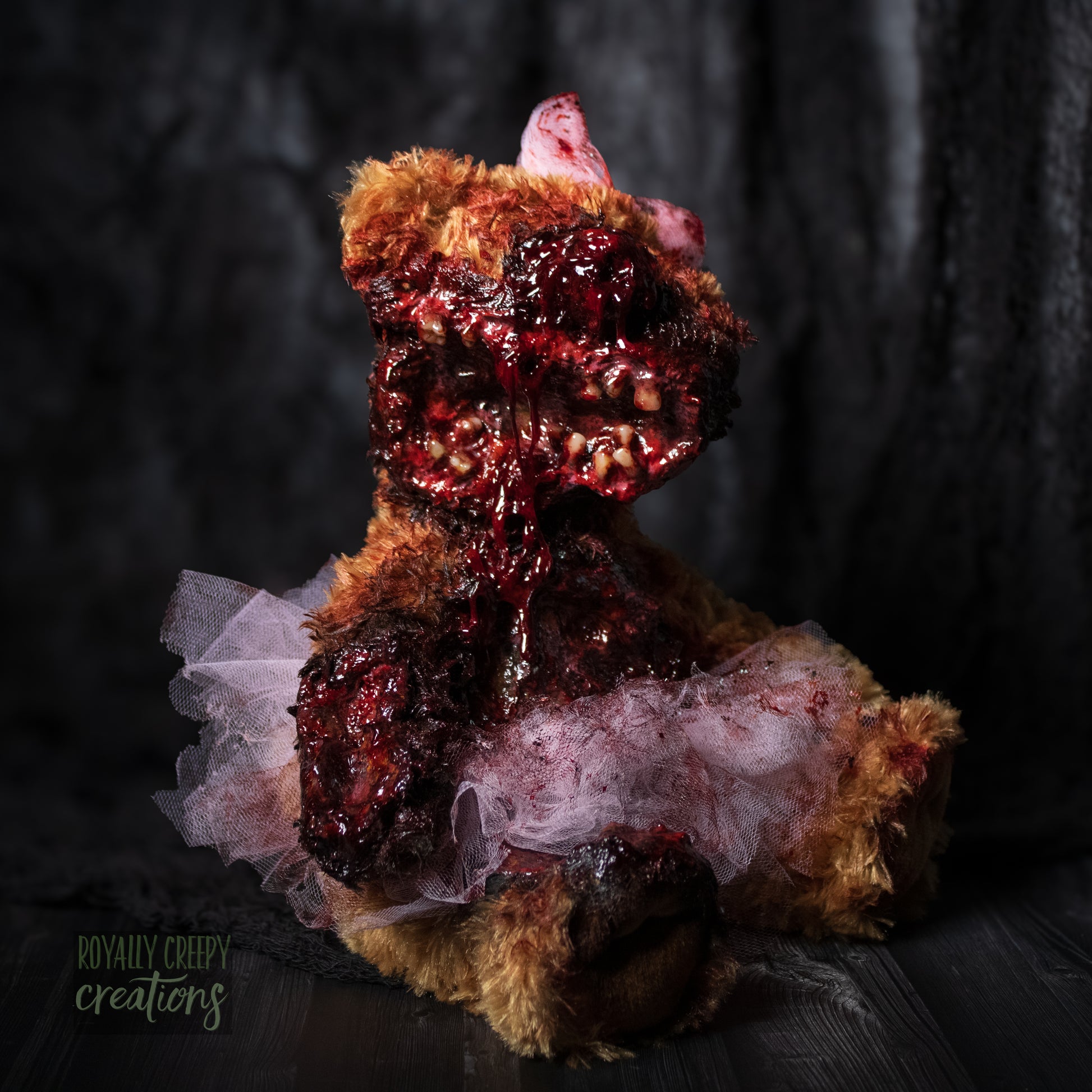 Right side view of horror teddy bear with exposed teeth, wearing a tutu & bow.