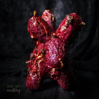 Close-up front of horror version of an infected balloon dog plushie covered in gore, maggots and flies.