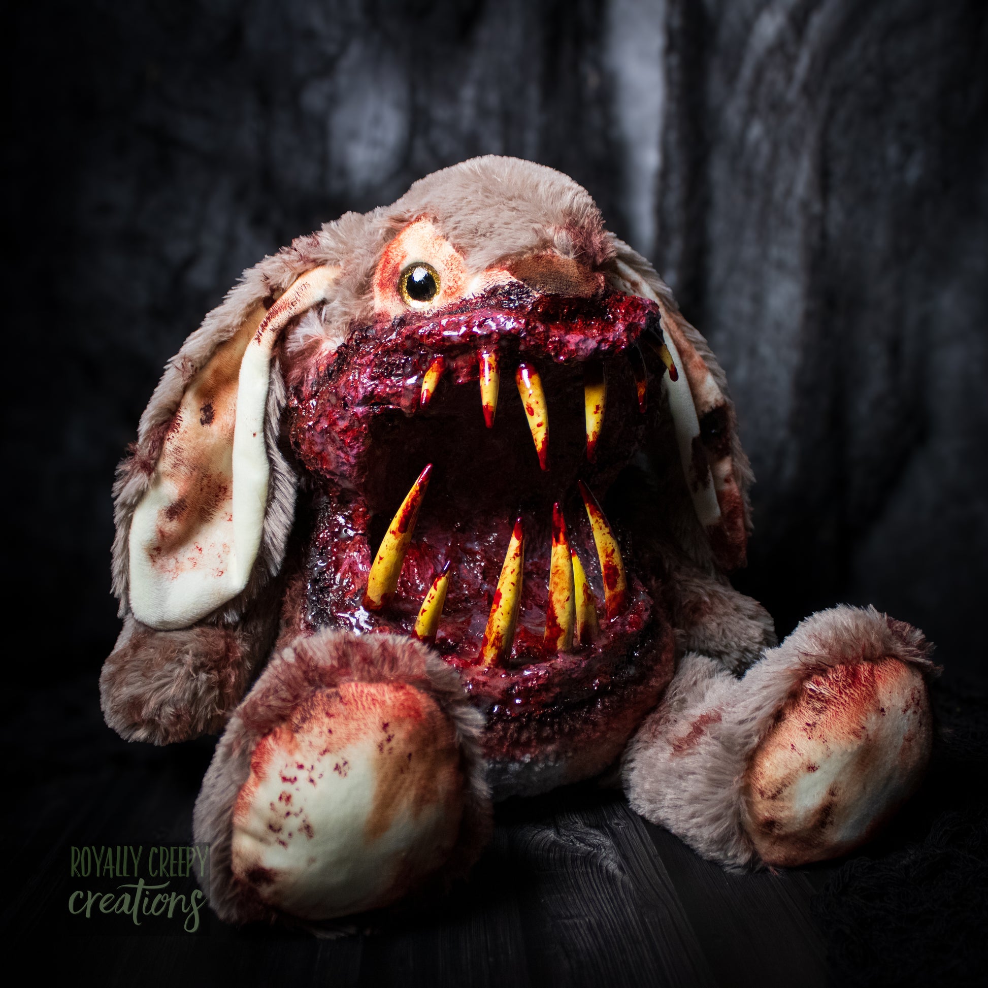Horror-themed bunny plushie with a grotesque mouth with big sharp teeth on a dark background.