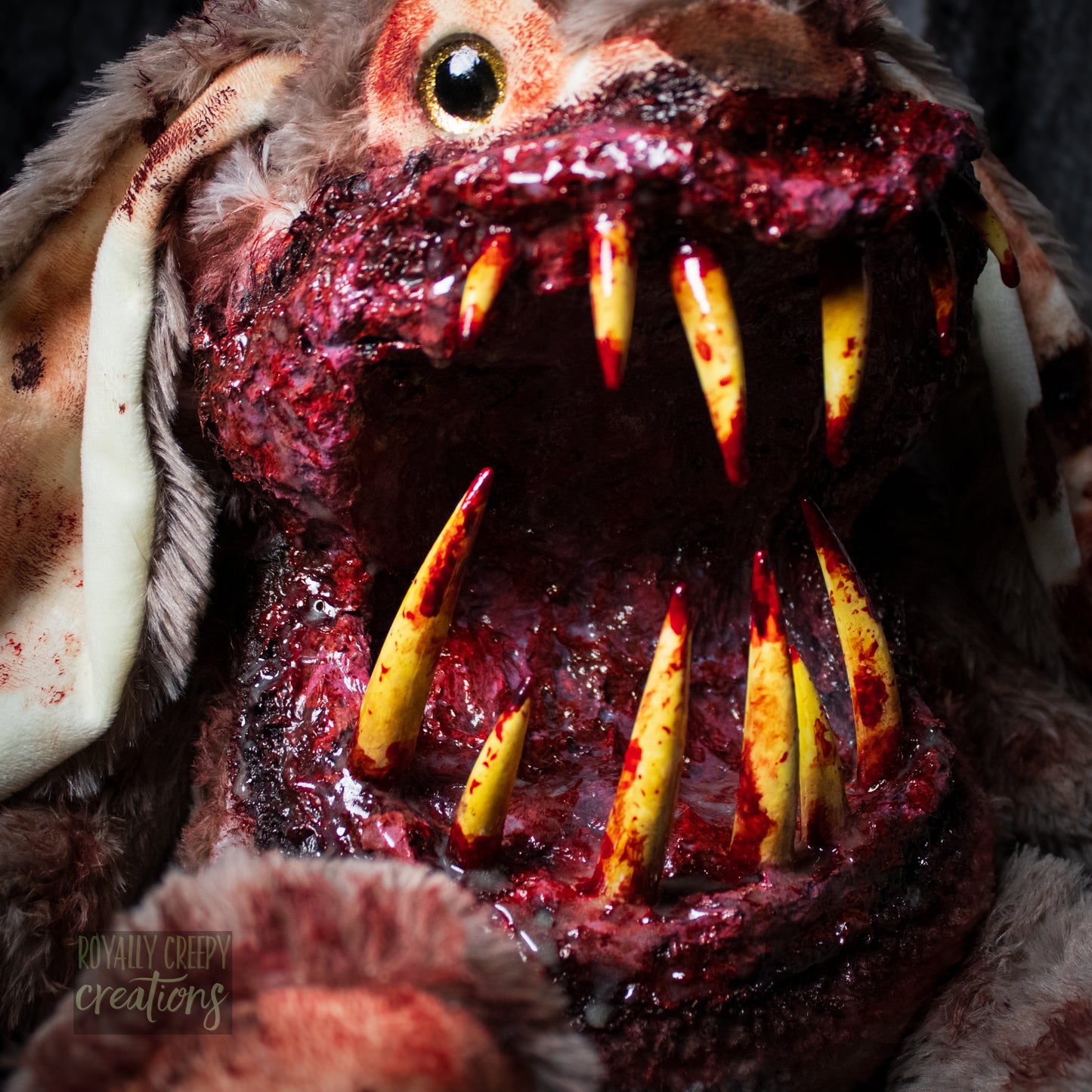 Close-up of horror-themed bunny plushie with a grotesque mouth with big sharp teeth on a dark background.