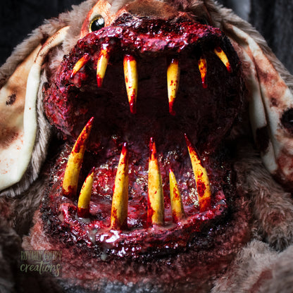 Close-up of horror-themed bunny plushie grotesque mouth with big sharp teeth on a dark background.