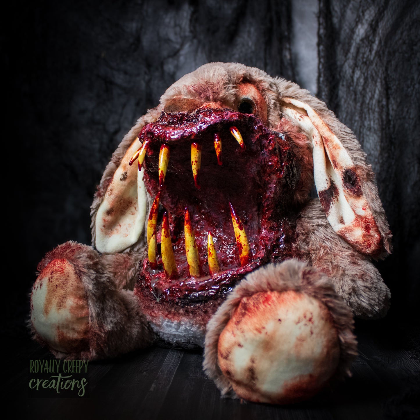 Angled side view of horror-themed bunny plushie with a grotesque mouth with big sharp teeth on a dark background.