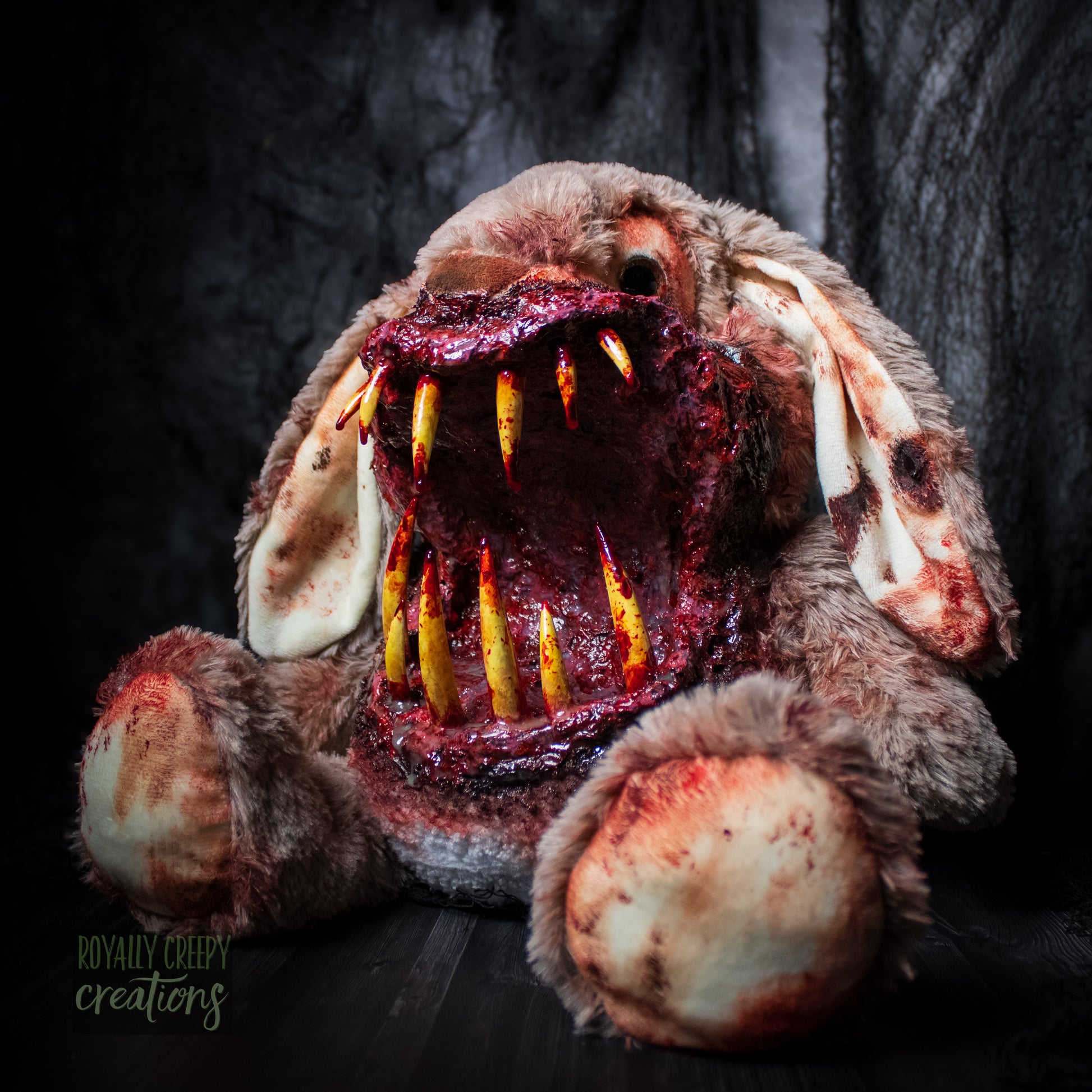 Angled side view of horror-themed bunny plushie with a grotesque mouth with big sharp teeth on a dark background.