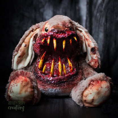 Front view of horror-themed bunny plushie with a grotesque mouth with big sharp teeth on a dark background.