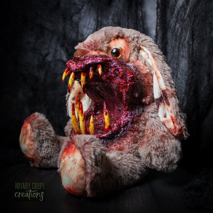 Left side of horror-themed bunny plushie with a grotesque mouth with big sharp teeth on a dark background.