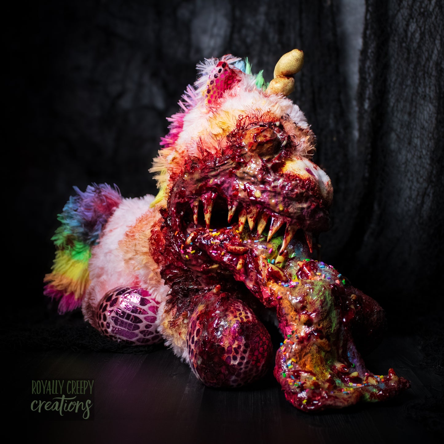 Horror themed unicorn plush with sharp teeth vomiting a rainbow covered with maggots and colorful sprinkles and fake blood.