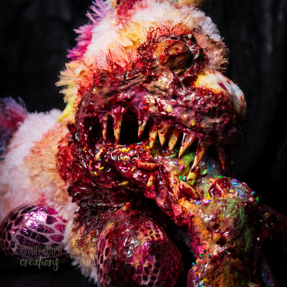 Close-up of a horror themed unicorn plush with sharp teeth vomiting a rainbow covered with maggots and colorful sprinkles and fake blood.