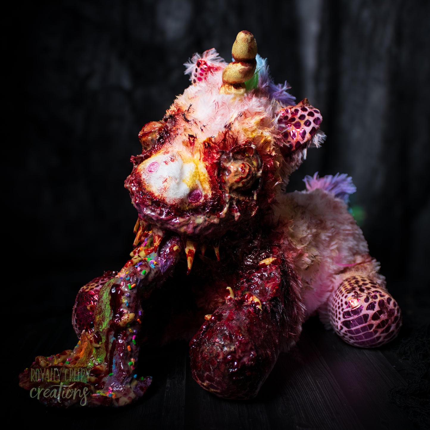 Another angle of horror unicorn plush vomiting a rainbow with a dark background.