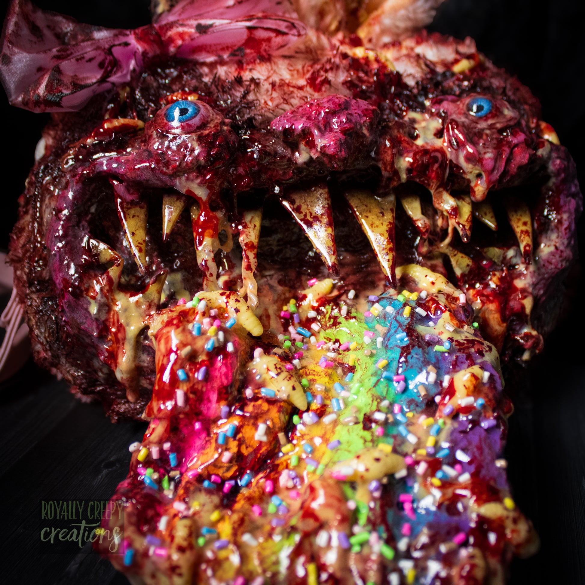 A close-up of a horror-themed bunny purse featuring a monstrous face with sharp teeth, blue eyes, a pink bow, and a colorful tongue covered in sprinkles, set against a dark background.