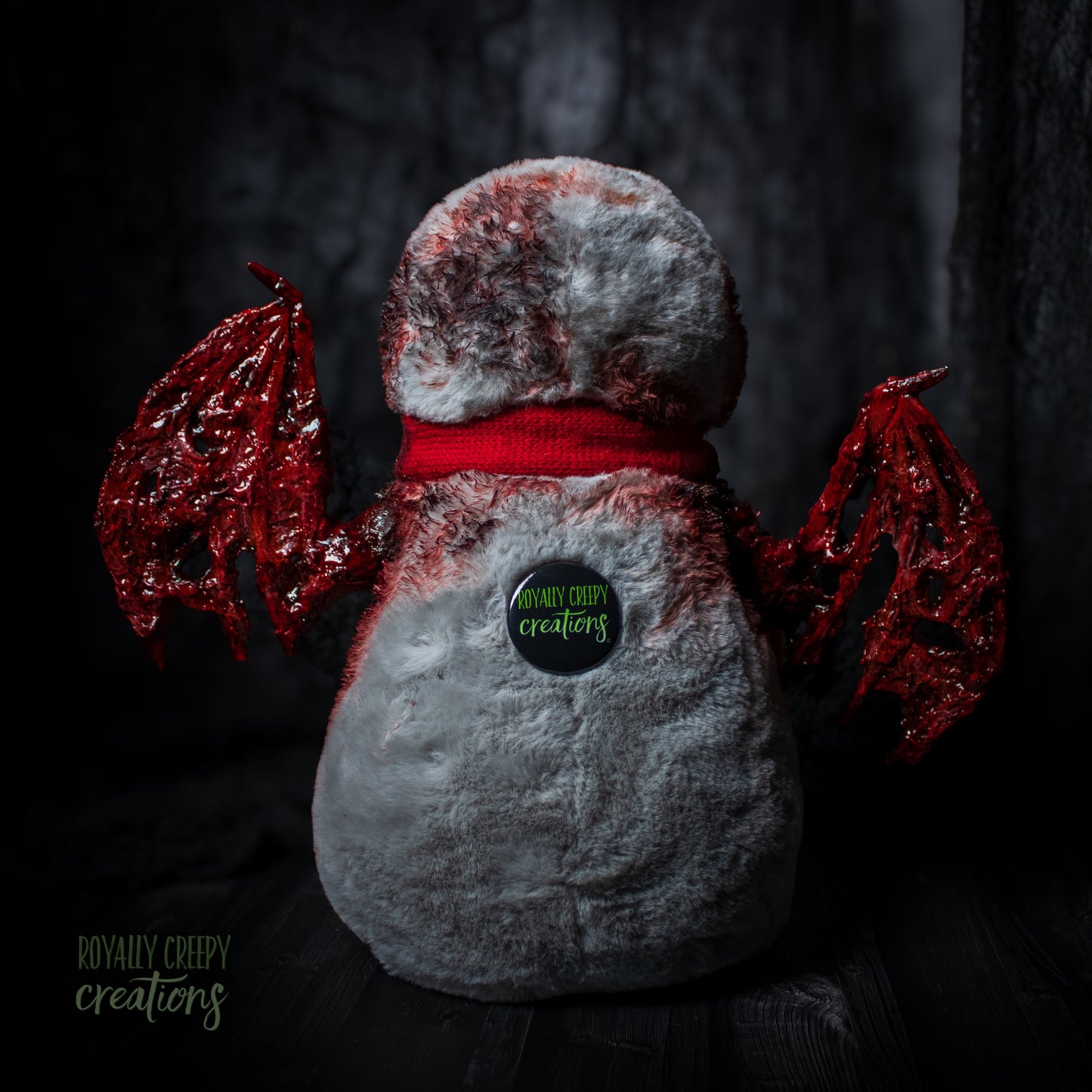 back of penguin with red wings and a red scarf on a dark background, featuring 'Royally Creepy Creations' logo.