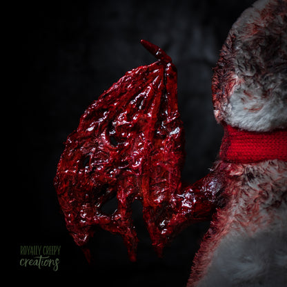 Close-up of a red textured bloody left wing attached to plush penguin with a red scarf on a dark background.