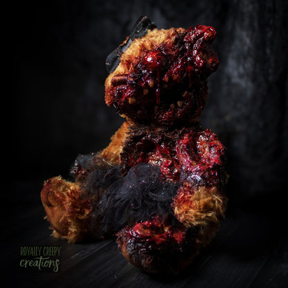 A horror-themed plush teddy bear with a grotesque, gory zombie-like face, bared teeth, and exposed flesh details, wearing a black tutu and black bow, set against a dark, moody background.