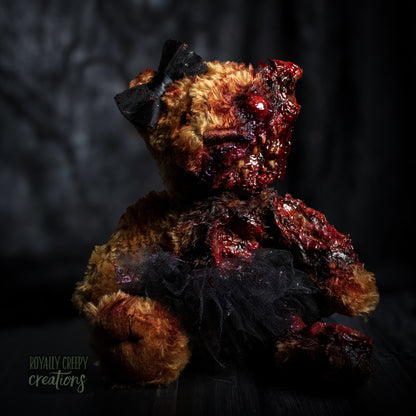 A horror-themed plush teddy bear with a grotesque, gory zombie-like face, bared teeth, and exposed flesh details, wearing a black tutu and black bow, set against a dark, moody background.