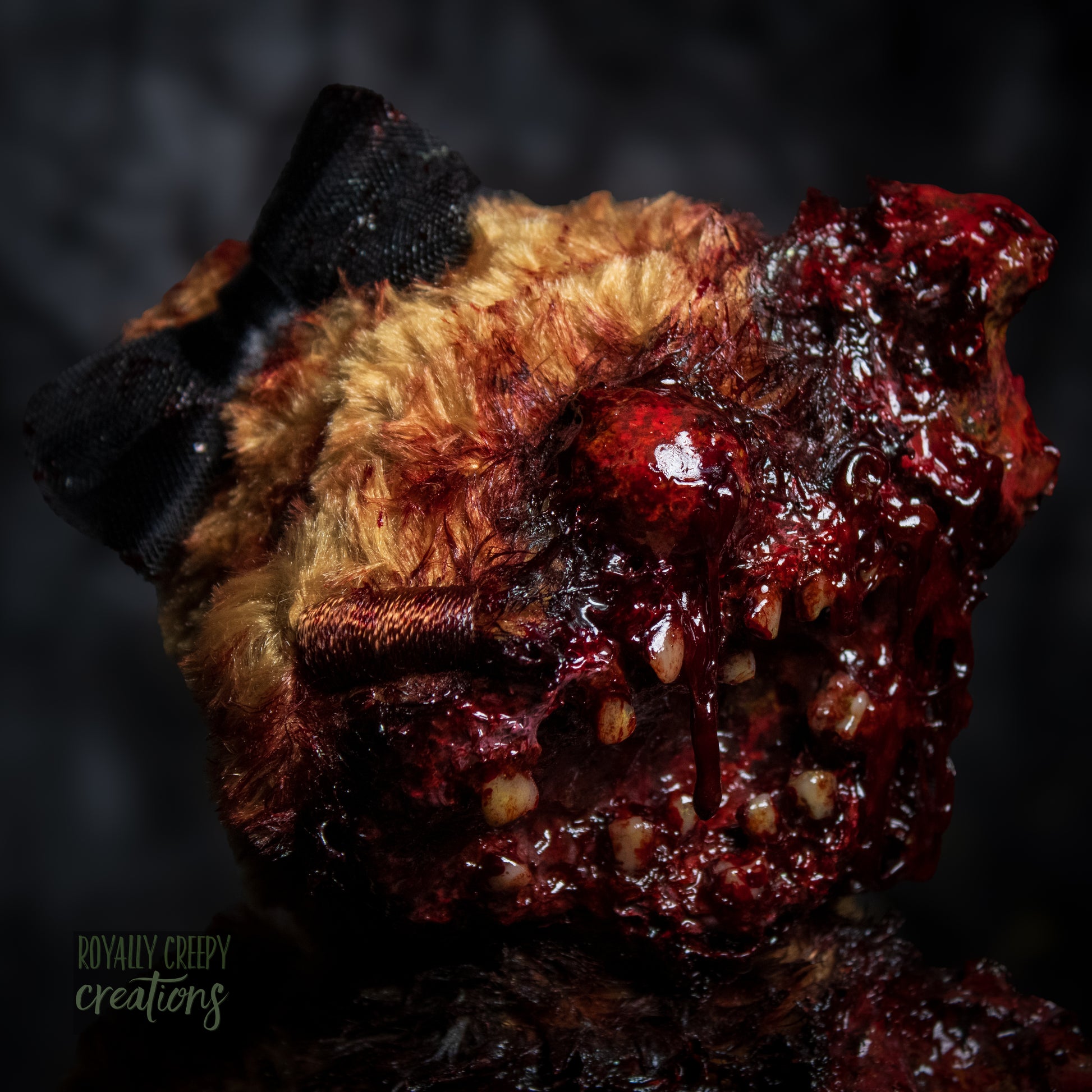 a close-up of a horror-themed plush teddy bear with a grotesque, gory zombie-like face, bared teeth, and exposed flesh details, set against a dark, moody background.