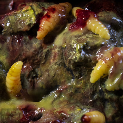 A close-up of a horror prop depicting a decaying, gory vomit  with yellow maggots embedded in it, covered in fake blood and green-yellow mold-like textures. A watermark for 'Royalty Creepy Creations' is visible in the bottom-left corner.