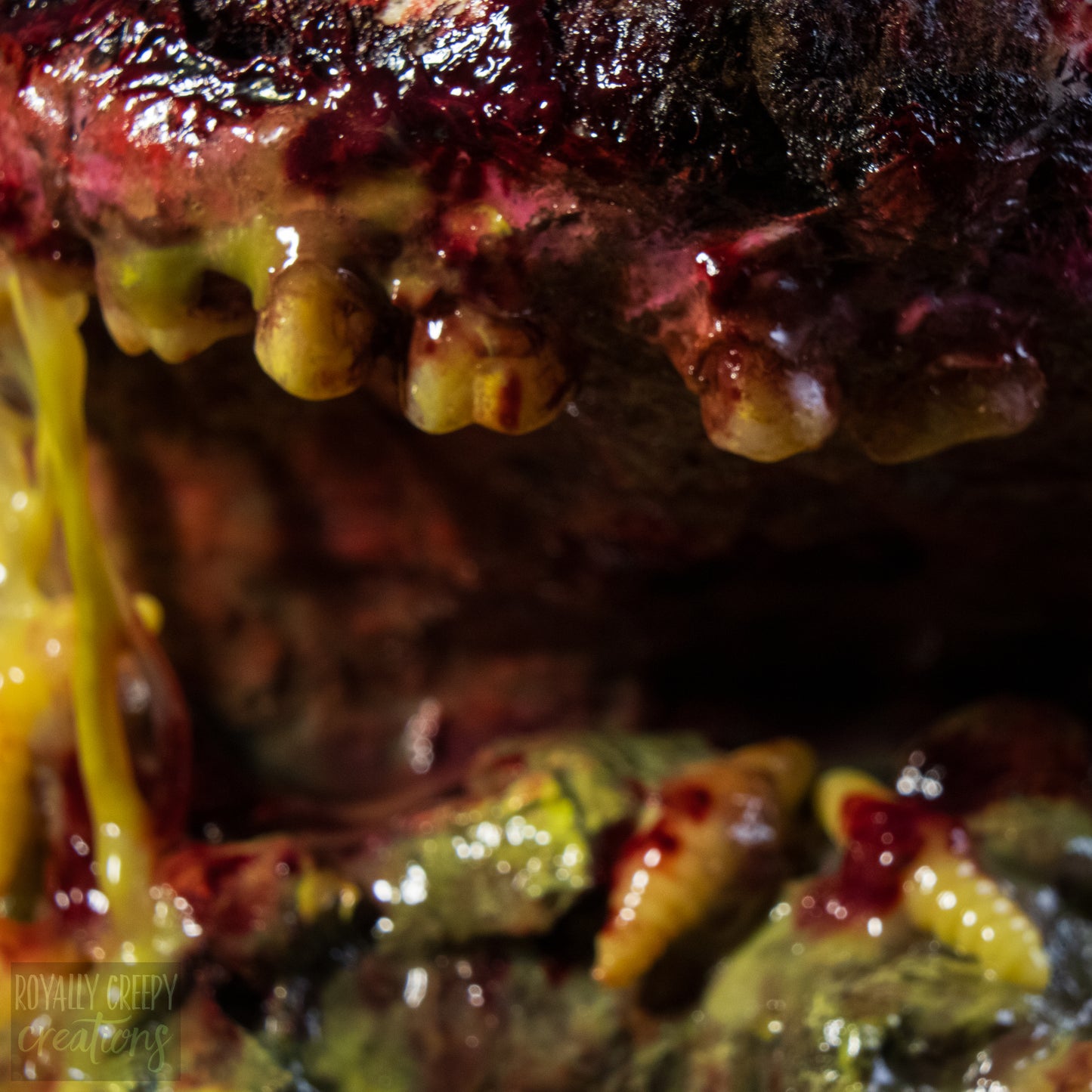 A close-up of a highly realistic fake severed mouth prop, featuring dark textured gums, yellow teeth, and dripping fake blood.