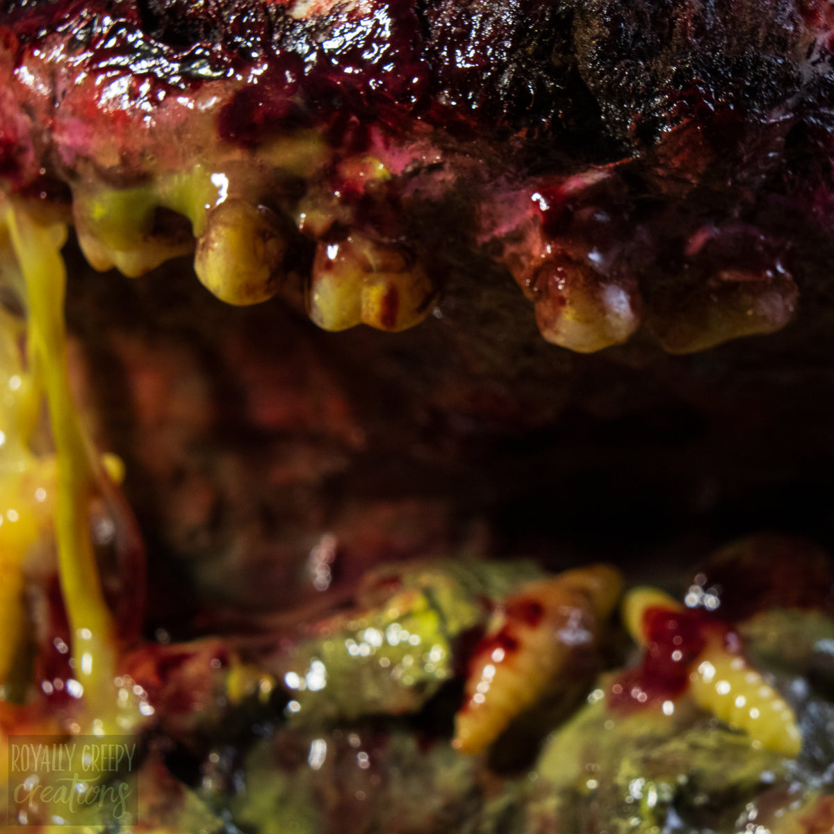 A close-up of a highly realistic fake severed mouth prop, featuring dark textured gums, yellow teeth, and dripping fake blood.