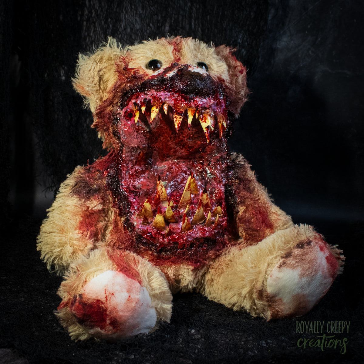 A horror-themed plush teddy bear with a grotesque, bloody mouth showing sharp yellowed teeth, set against a dark textured background.