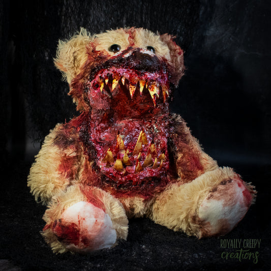 A horror-themed plush teddy bear with a grotesque, bloody mouth showing sharp yellowed teeth, set against a dark textured background.