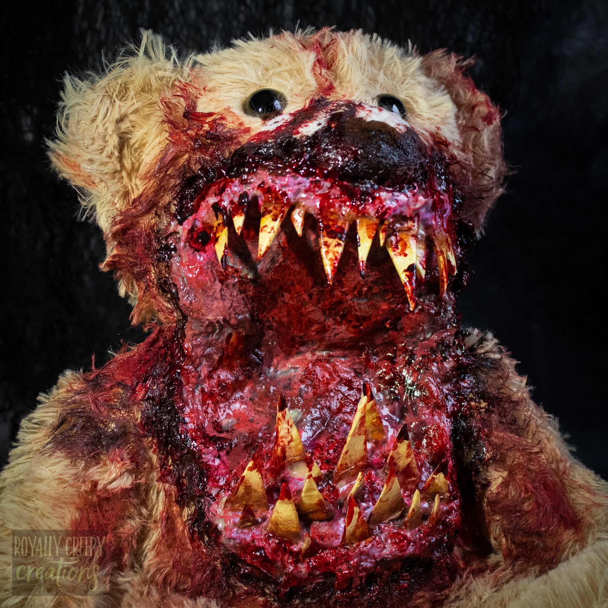A close-up of a horror-themed plush teddy bear with a grotesque, bloody mouth showing sharp yellowed teeth, set against a dark textured background.