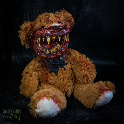 A horror-themed plush teddy bear with a grotesque bloody mouth showing yellowed teeth, sitting against a dark background. 
