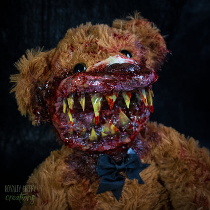 A close-up of a horror-themed plush teddy bear with a grotesque bloody mouth showing yellowed teeth, sitting against a dark background. 