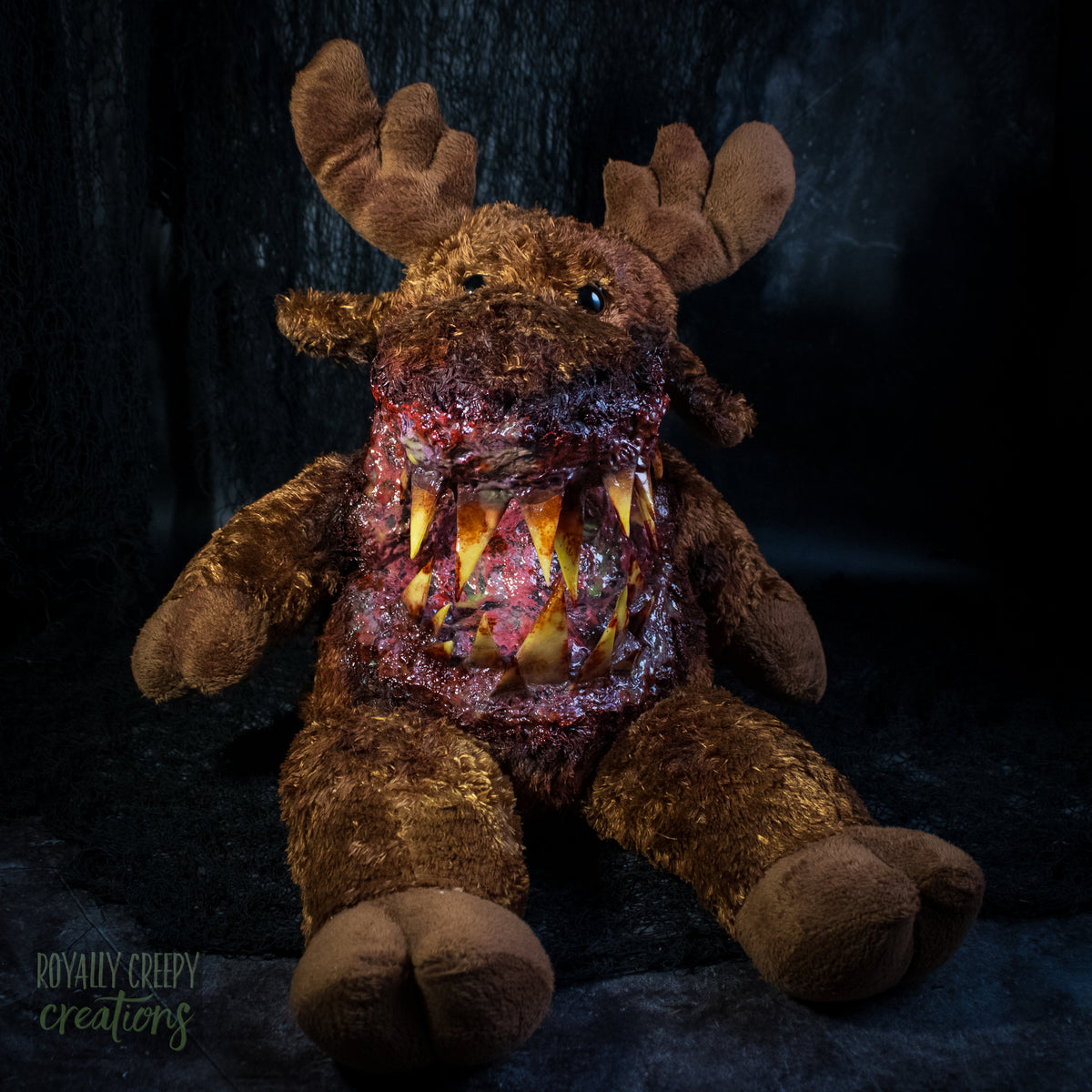 A creepy moose plush toy with a horror zombie-like mouth, showing exposed flesh and sharp yellowed teeth, set against a dark textured background.