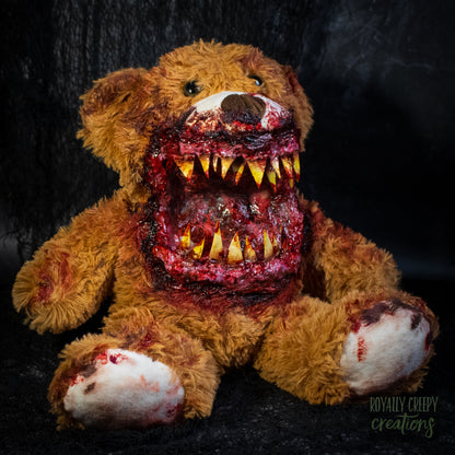 A horror-themed plush teddy bear with a grotesque, bloody open mouth showing sharp yellow teeth, set against a dark textured background.