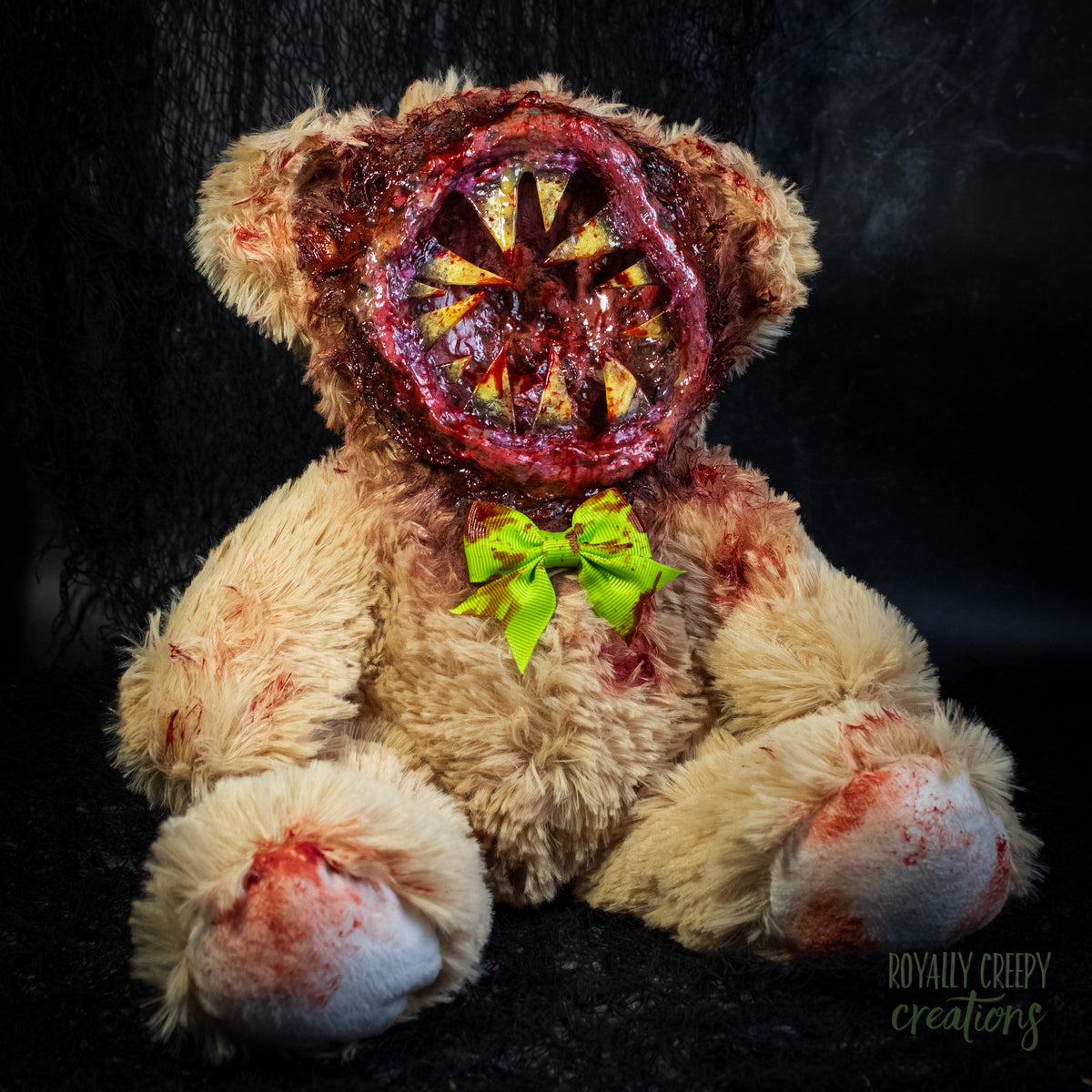 A horror-themed plush teddy bear with a  big round grotesque mouth covering it's face. Big sharp yellow teeth and blood splatter detail. 