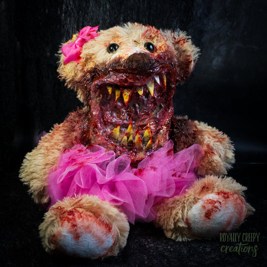 A horror-themed plush teddy bear with a bloody, grotesque mouth showing sharp teeth, a bright pink tutu, and a pink bow on its head, set against a dark background.