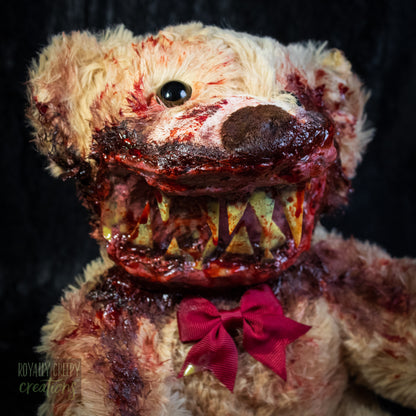 A horror-themed plush teddy bear with a bloody mangled face, sharp teeth, and a red bow tie, photographed against a black background.