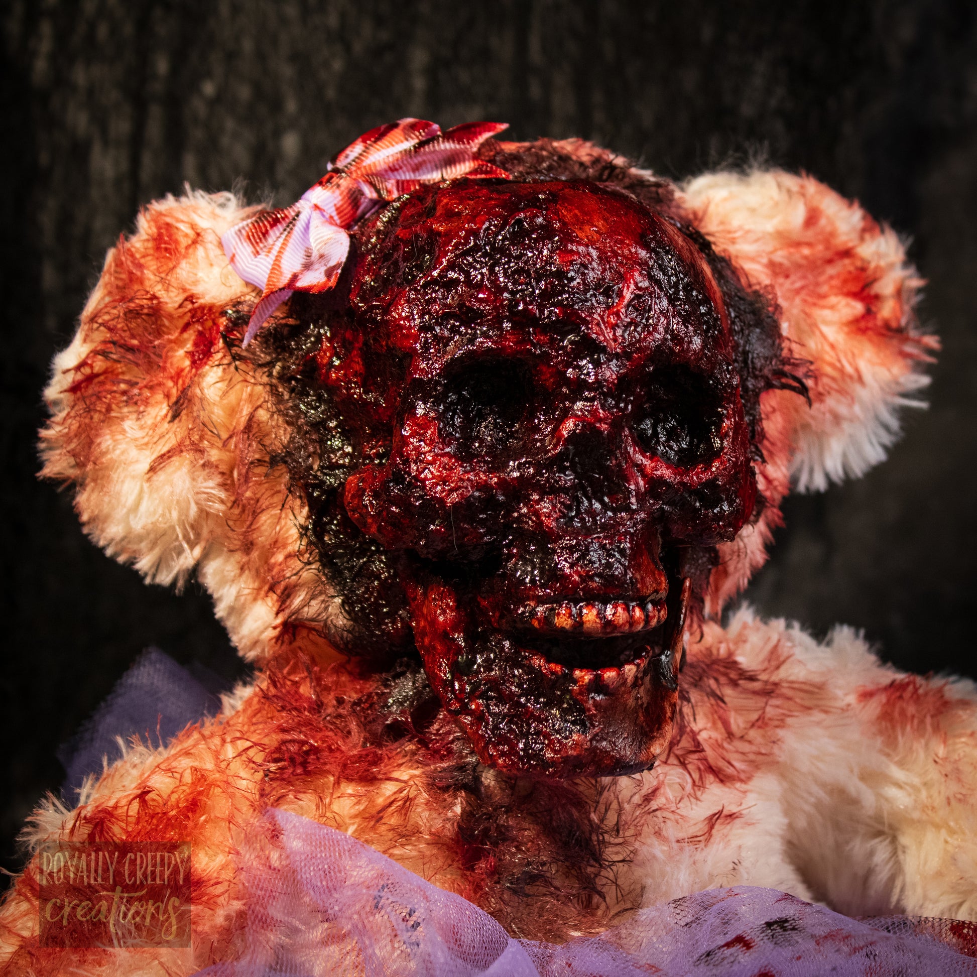 A horror-themed plush teddy bear with a bloody, skull-like face, blood-splattered fur, and a small pink bow on its head, set against a dark textured background.