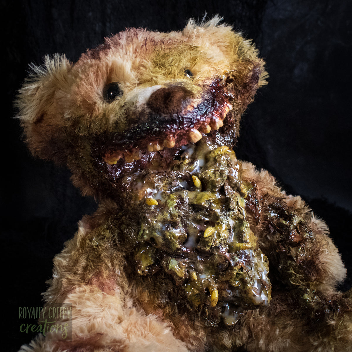 Close-up of a horror-themed plush teddy bear with a grotesque, decayed mouth and exposed vomit set against a dark textured background. A 'Royally Creepy Creations' watermark is visible in the bottom corner.