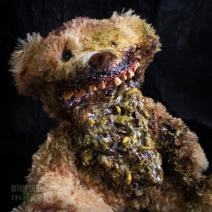 Close-up of a horror-themed plush teddy bear with a grotesque, decayed mouth and exposed vomit set against a dark textured background. A 'Royally Creepy Creations' watermark is visible in the bottom corner.