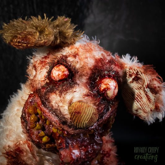 A close-up of a  horror-themed zombie dog plush toy with tattered fur, bloodshot red eyes, a bloody gaping mouth.